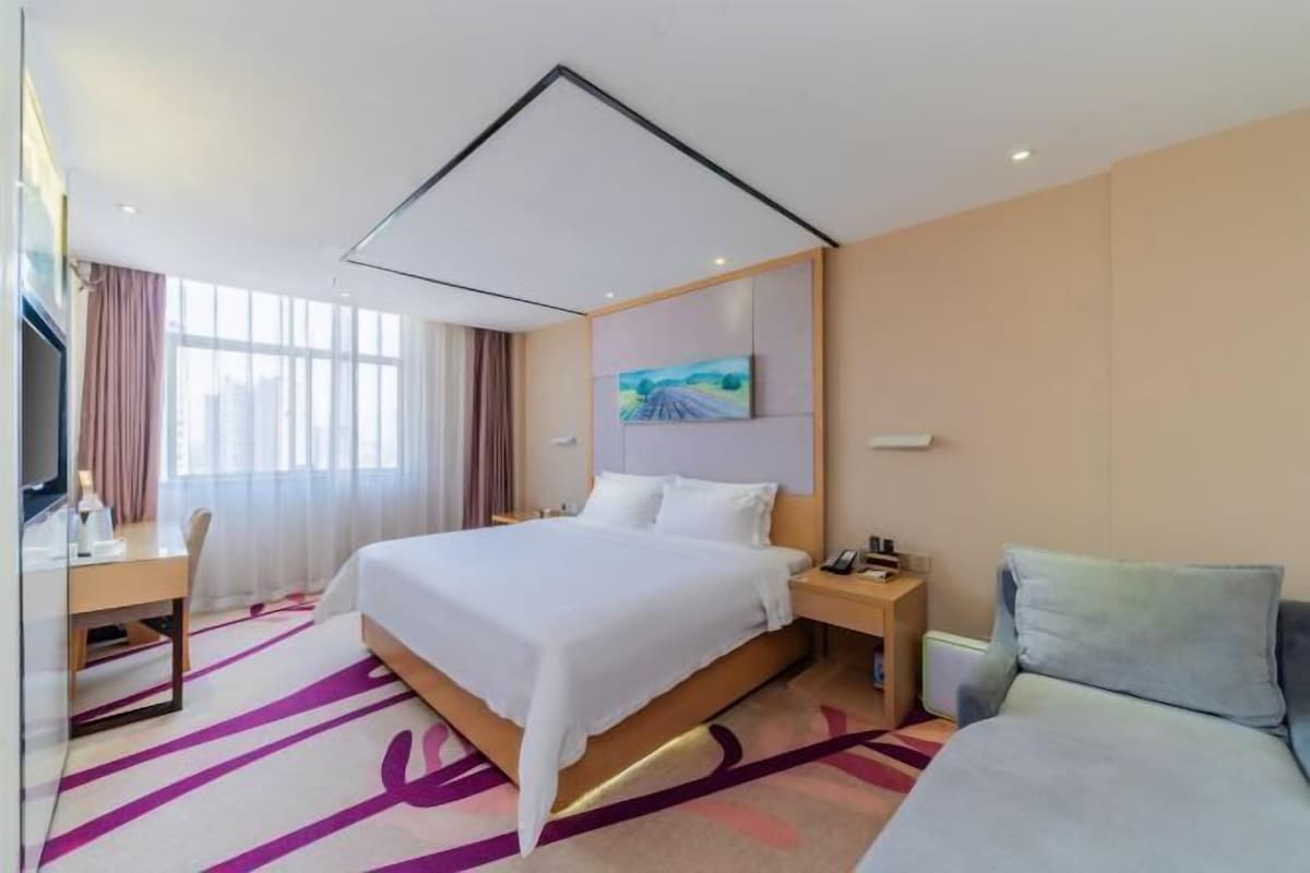 A hotel room with a large bed, a desk, a chair, a TV, and a painting on the wall.