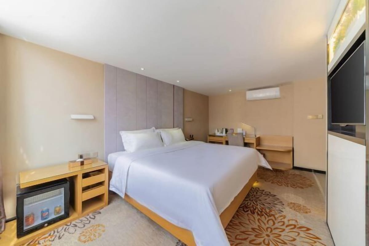 A hotel room with a bed, bedside tables, a TV, and a carpeted floor.