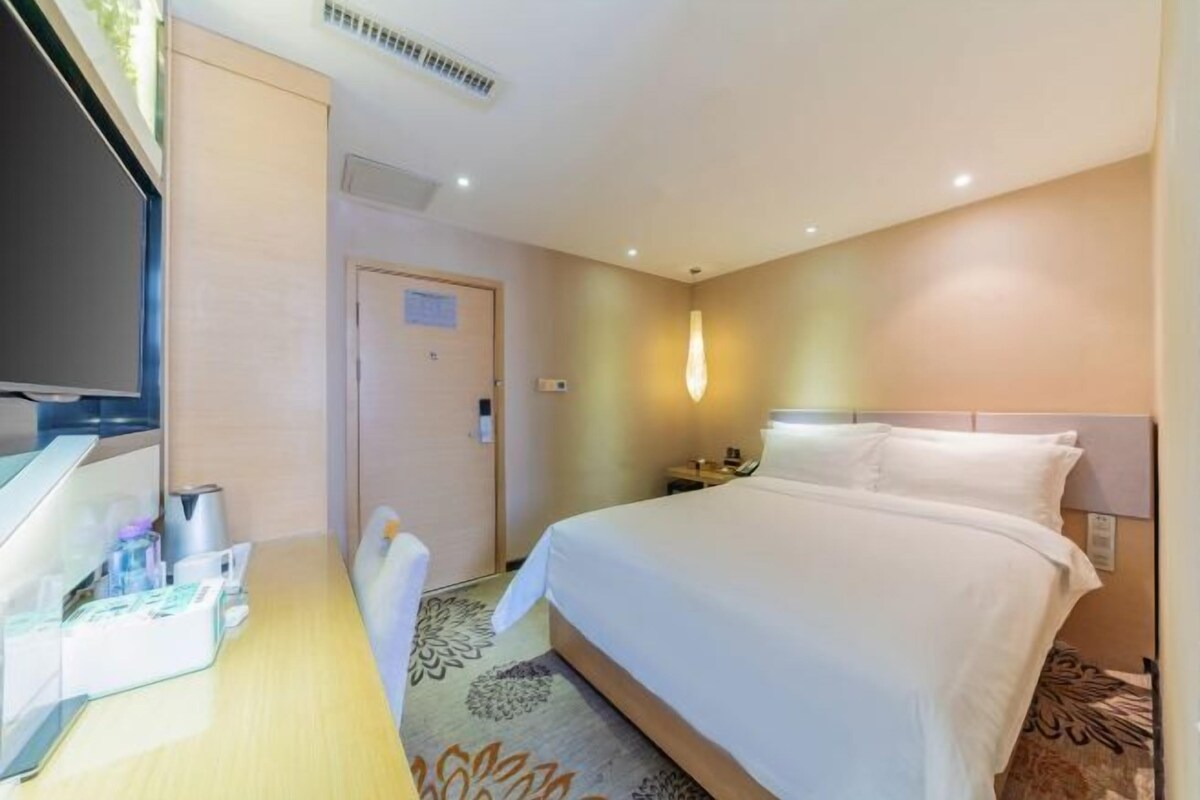 A hotel room with a bed, bedside table, lamp, and a television on a desk.