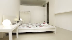 Ein schlicht eingerichtetes Schlafzimmer mit einem weißen Bett, einem Nachttisch mit Lampe und einem Spiegel.