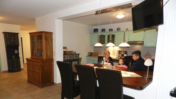 A dining area with a wooden table, black chairs, and a kitchen in the background. - Assisihof - Apartment zur Linde (Friedeburg)