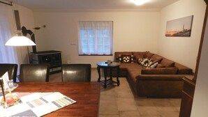 A living room with a wooden dining table, a sofa, and a small round table. - Assisihof - Apartment zur Linde (Friedeburg)