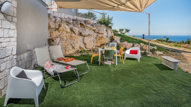 An outdoor patio with a table and chairs, a stone wall, and a view of the sea. - Apt Mari E Monti A 2 Km Da Riserva Dello Zingaro (Castellammare del Golfo)