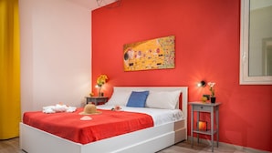 A bedroom with a red wall, a white bed, and a painting above it. - Apt Mari E Monti A 2 Km Da Riserva Dello Zingaro (Castellammare del Golfo)
