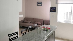 A kitchen with a granite countertop, a dining table with chairs, a sofa, and a window with blinds. - Cozy Apartment in the City of Morelia (Morelia)