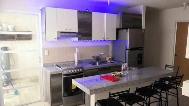 A modern kitchen with a central island, stainless steel appliances, and blue under-cabinet lighting. - Cozy Apartment in the City of Morelia (Morelia)