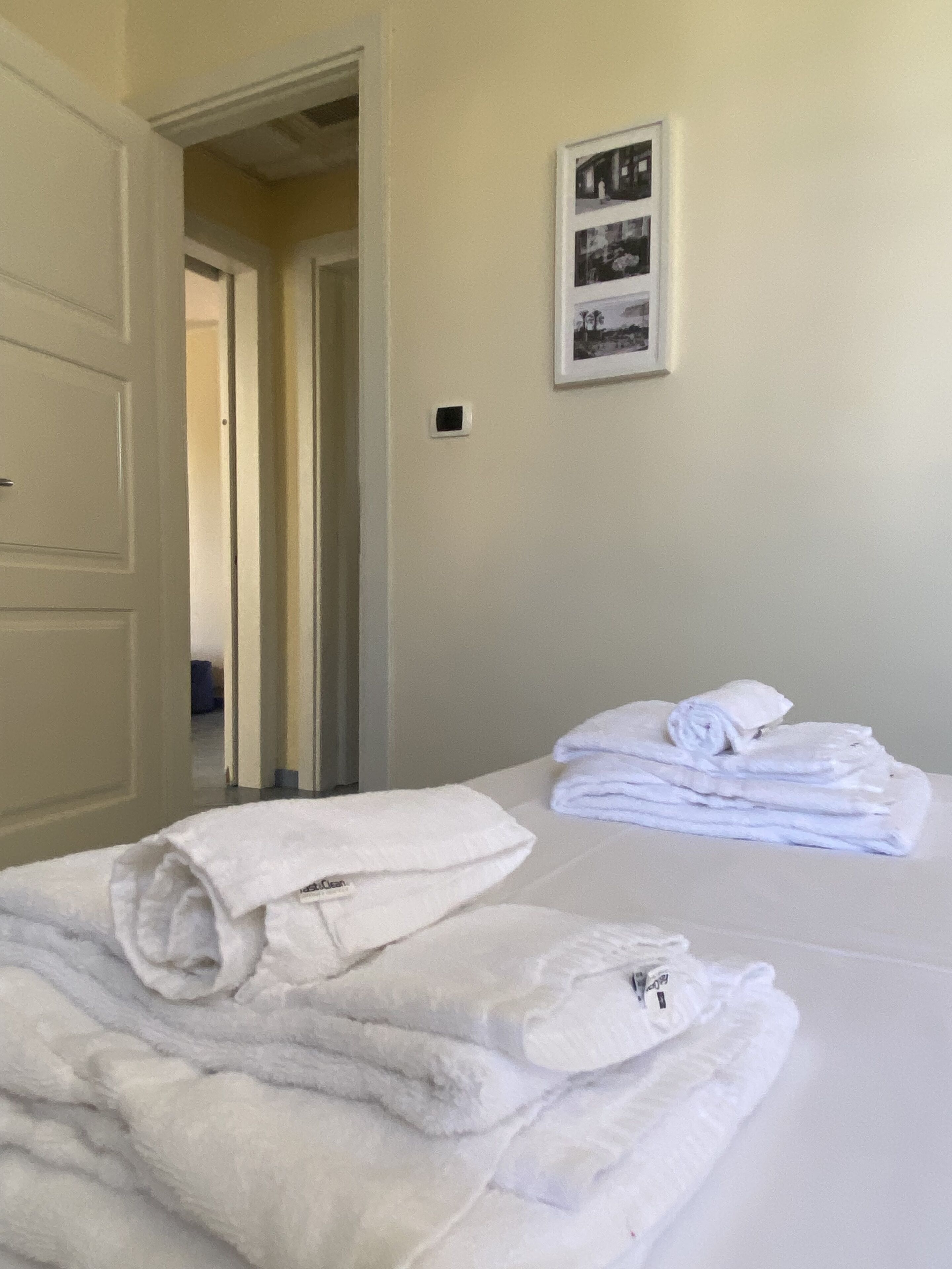 Une chambre d’hôtel avec un lit soigneusement fait, une pile d’serviettes et une photo encadrée accrochée au mur.
