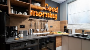 Una cucina moderna con lavastoviglie, forno e macchina da caffè integrati. Sopra il lavello si trova una mensola in legno e un cartello con la scritta 'Good morning'.