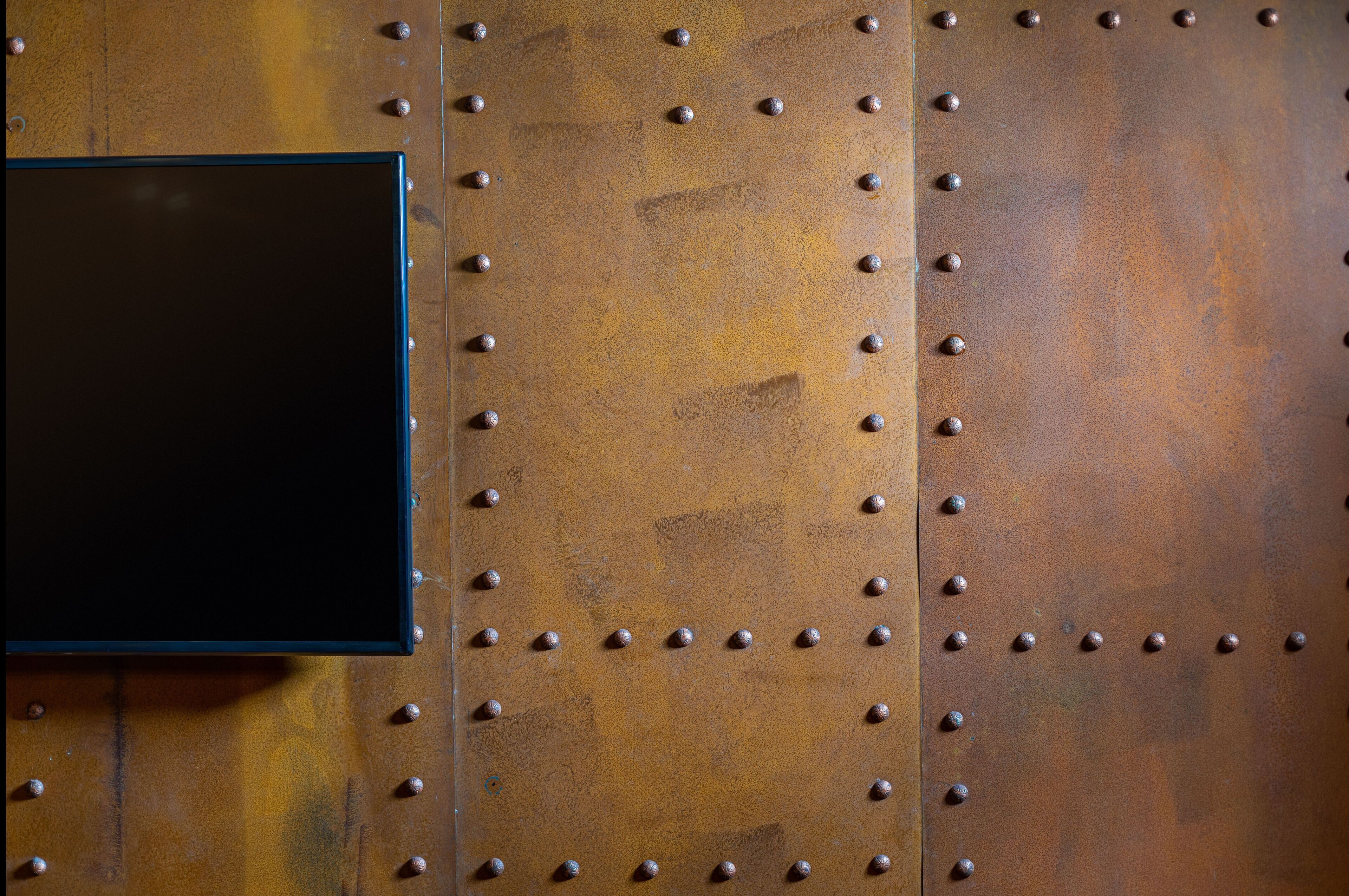 A close-up of a metallic wall with rivets and a black rectangular object.