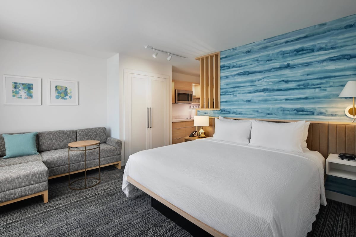 Hotellihuone, jossa on suuri sänky, sohva, pieni pyöreä pöytä ja seinällä taulu.