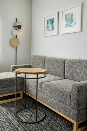 A modern living room with a grey sofa, a round wooden coffee table, and two abstract paintings on the wall. - TownePlace Suites Tampa Casino Area (Tampa)