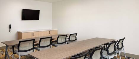A conference room with a long table, six chairs, a flat-screen TV mounted on the wall, and a wooden cabinet.