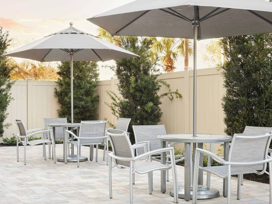 An outdoor patio with round tables and chairs, large umbrellas, and a beige fence.