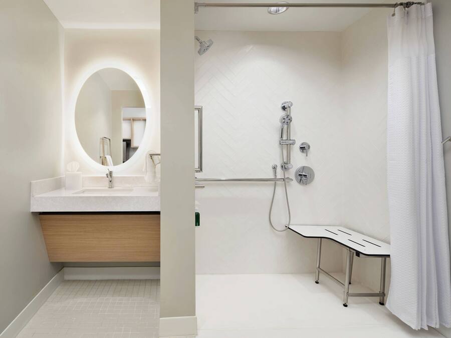 A modern bathroom with a vanity, a shower with a handheld showerhead, and a white bench.