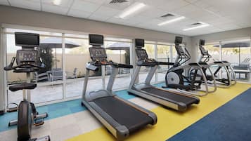 Un gimnasio con cintas de correr, elípticas y una bicicleta estática, ventanas amplias y vistas al exterior.