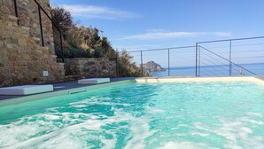 A swimming pool with clear blue water, surrounded by stone walls and a wooden deck. - La Villa Del Borgo Cefalù (Cefalù)