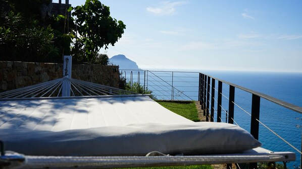 A hammock with a cushion on a balcony overlooking the sea.