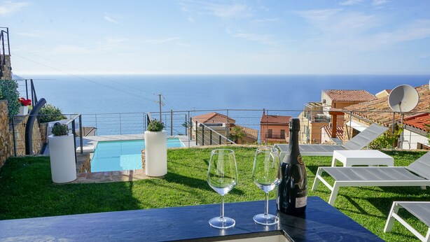 A poolside view with a clear view of the sea, a bottle of wine, and two glasses on a table. - La Villa Del Borgo Cefalù (Cefalù)
