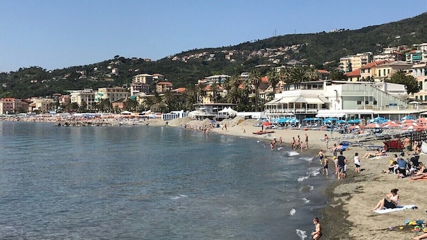 A coastal beach with people sunbathing and swimming, surrounded by buildings and hills. - PRETTY AND VERY CENTRAL ATTIC ONE STEP FROM THE SEA (Varazze)
