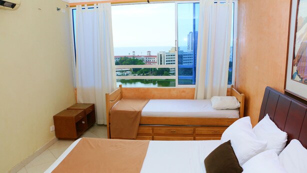 A hotel room with a large bed, a smaller bed, a window with a view of buildings and a body of water, and a wooden headboard. - Sea View Apartment 1-11c air Wifi (Cartagena)