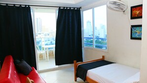 A room with a bed, a red couch, and a view of the city through large windows. - Sea View Apartment 1-11c air Wifi (Cartagena)