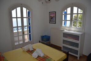 A room with a bed, a window with a view, a radiator, and a blue storage bin. - Villa Iokasti Sea View (Corinth)