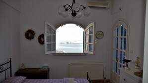 A bedroom with a bed, a nightstand, a dresser, a window with an open shutter, a radiator, and a wall clock. - Villa Iokasti Sea View (Corinth)