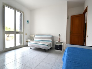 Une chambre à coucher avec un lit, une chaise, une table de chevet, une lampe et une porte.