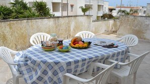 A table set on a rooftop terrace with a checkered tablecloth, surrounded by white plastic chairs. - Charming Holiday Home Near The Beach With A Terrace, Pets (Melendugno)