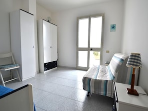 Une pièce comprenant un lit, une table de chevet avec une lampe, une armoire, une chaise et une porte donnant sur l’extérieur.