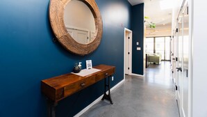 A hallway with a wooden console table, a large round mirror, and a door leading to a room with a plant and a sofa. - Broken Hill Designer Baker St Flat Mountain View.  (Nelson)