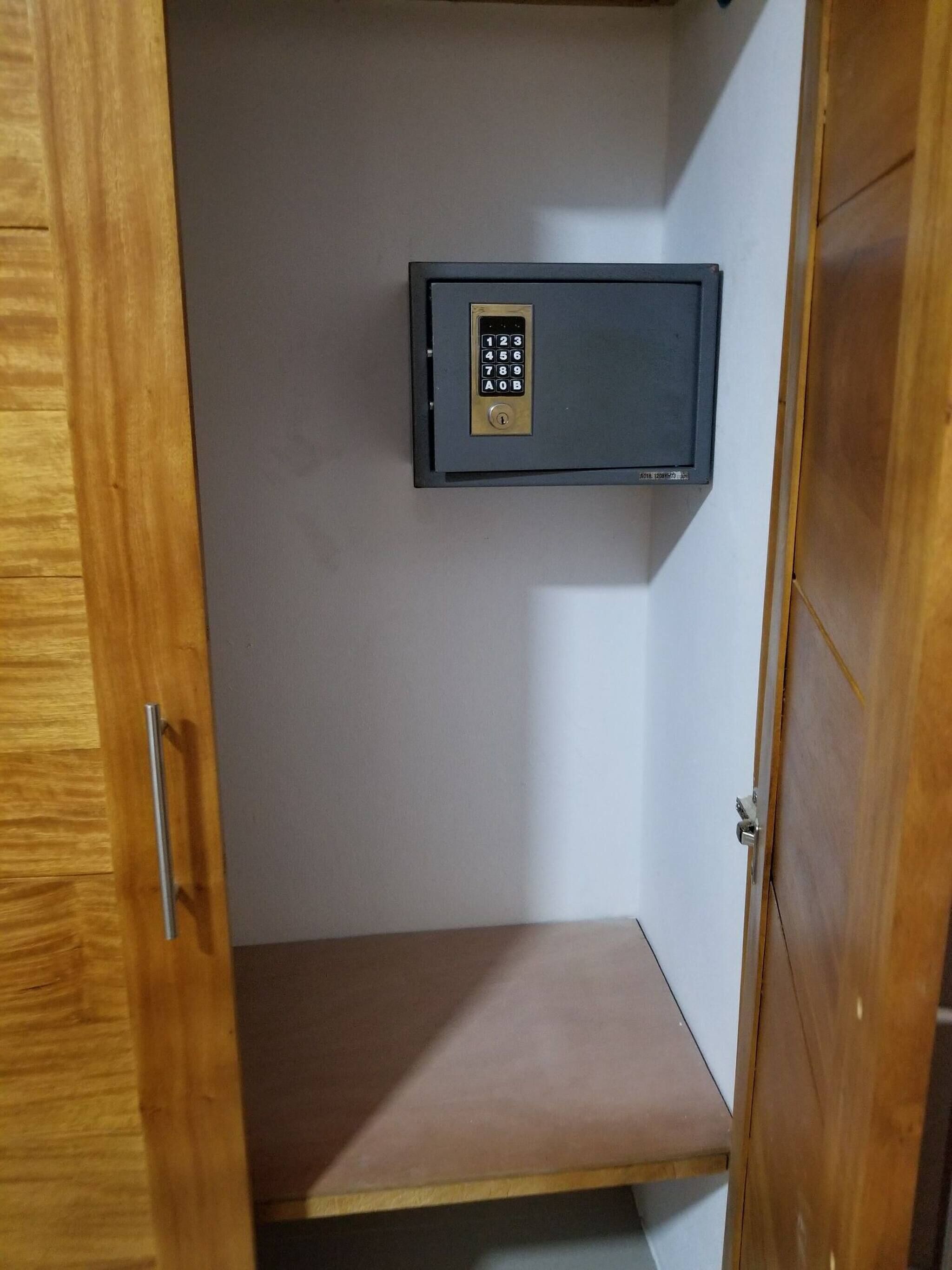 Une pièce avec une porte en bois, une petite étagère et un coffre-fort fixé au mur.