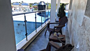 A balcony with two chairs, a small table with a glass, and a view of a pool and buildings. - Charming 1b Apto Walk To The Beaches & Main Street (Sosúa)