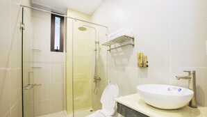 Un baño moderno con ducha envuelta en vidrio, inodoro blanco y un lavamanos tipo cuenco grande.