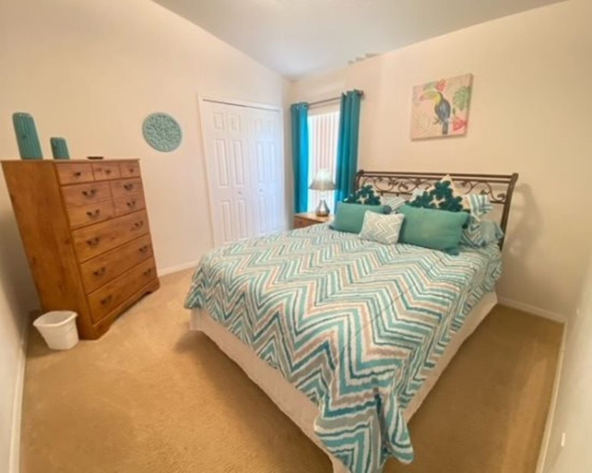 A bedroom with a bed, a dresser, a door, and a wall with a painting.