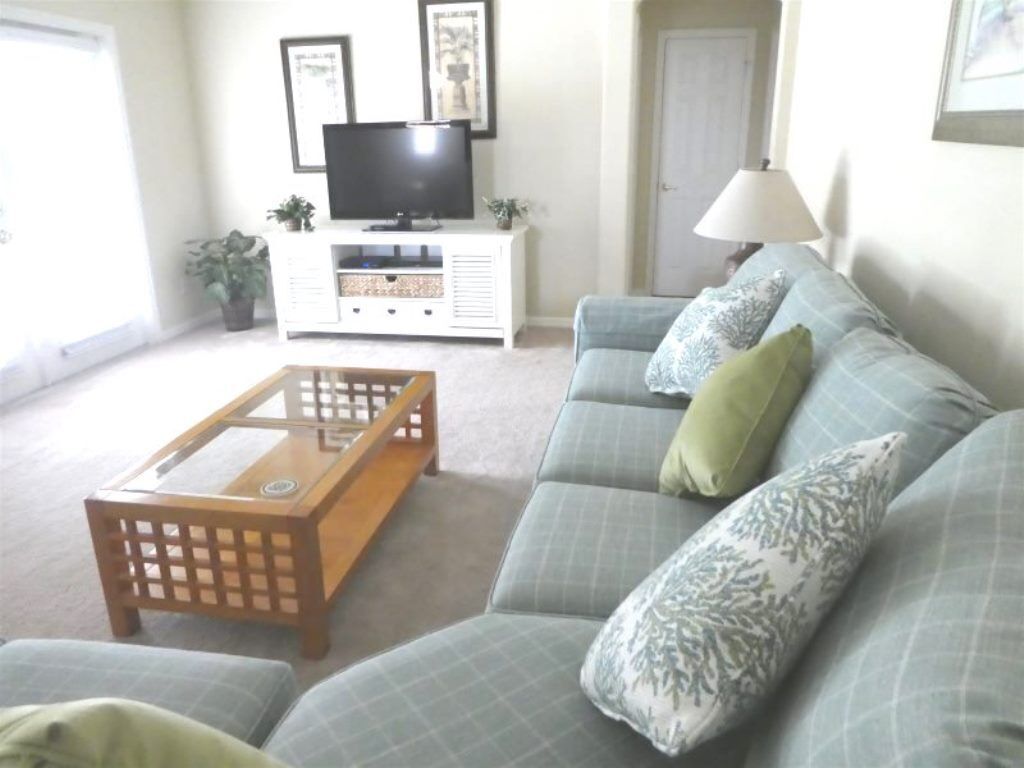 A living room with a sofa, a coffee table, a TV on a stand, and a lamp.