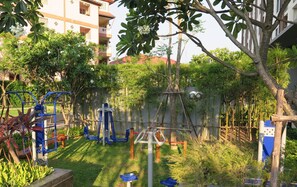 Un parque infantil con aparatos de ejercicio, rodeado de vegetación y edificios residenciales.