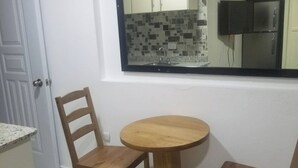 A small dining area with a round wooden table and two chairs, a fan, and a tiled backsplash. - 2 Guests 1bed Studio 3min To Beach And Main Street (Sosúa)