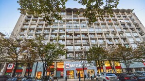 Un immeuble à plusieurs étages doté de balcons, une devanture de magasin avec une enseigne et des voitures garées.