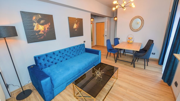 Un salon moderne avec un canapé bleu, une table basse en verre et un coin repas comprenant une table et des chaises en bois.