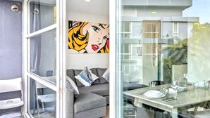 Un intérieur moderne avec une table à manger en verre, un canapé gris et une fresque murale colorée de style pop art.