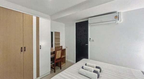 A bedroom with a bed, a wardrobe, a desk, and an air conditioning unit.