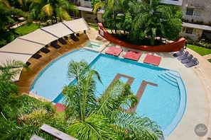 A pool area with lounge chairs and umbrellas, surrounded by greenery and a building in the background. - Spacious Ph 3 Bedrooms With Private Terrace, Beach Club Access (Playa del Carmen)