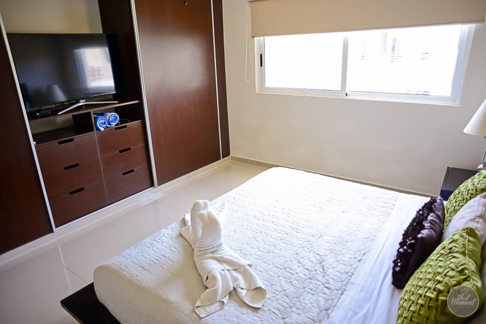Une chambre à coucher avec un lit, un téléviseur posé sur un meuble, une armoire et une fenêtre.