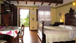 A room with a bed, a table with a floral tablecloth, and a chair. There is a wooden ceiling and a door leading outside. - Podere Caldaruccio La Pineta - Bungalow (Perugia)