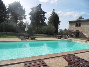 A swimming pool with lounge chairs and umbrellas, surrounded by trees and a stone building.