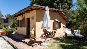A small, single-story building with a patio area featuring a table and chairs, a white umbrella, and two lounge chairs. - Podere Caldaruccio La Pineta - Bungalow (Perugia)
