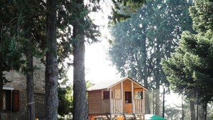A wooden playhouse with a ramp and slide, surrounded by trees and a hammock. - Podere Caldaruccio La Pineta - Bungalow (Perugia)