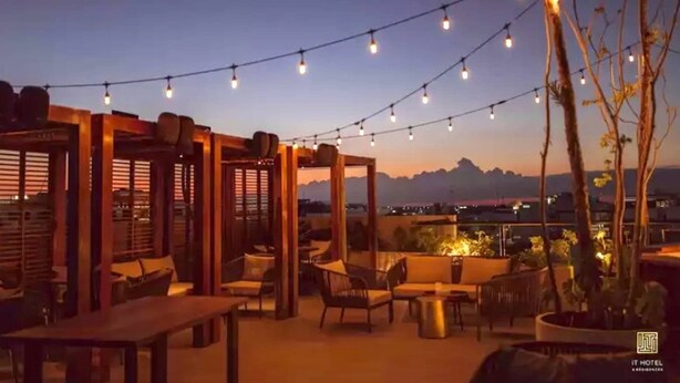 An outdoor seating area with string lights, wooden pergolas, and a view of the mountains at dusk. - It Residence, 2 Bedroom Apartment with Rooftop Pool (Playa del Carmen)