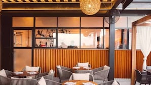 An outdoor seating area with wicker chairs and round tables, wooden slats on the wall, and a hanging light fixture. - It Residence, 2 Bedroom Apartment with Rooftop Pool (Playa del Carmen)